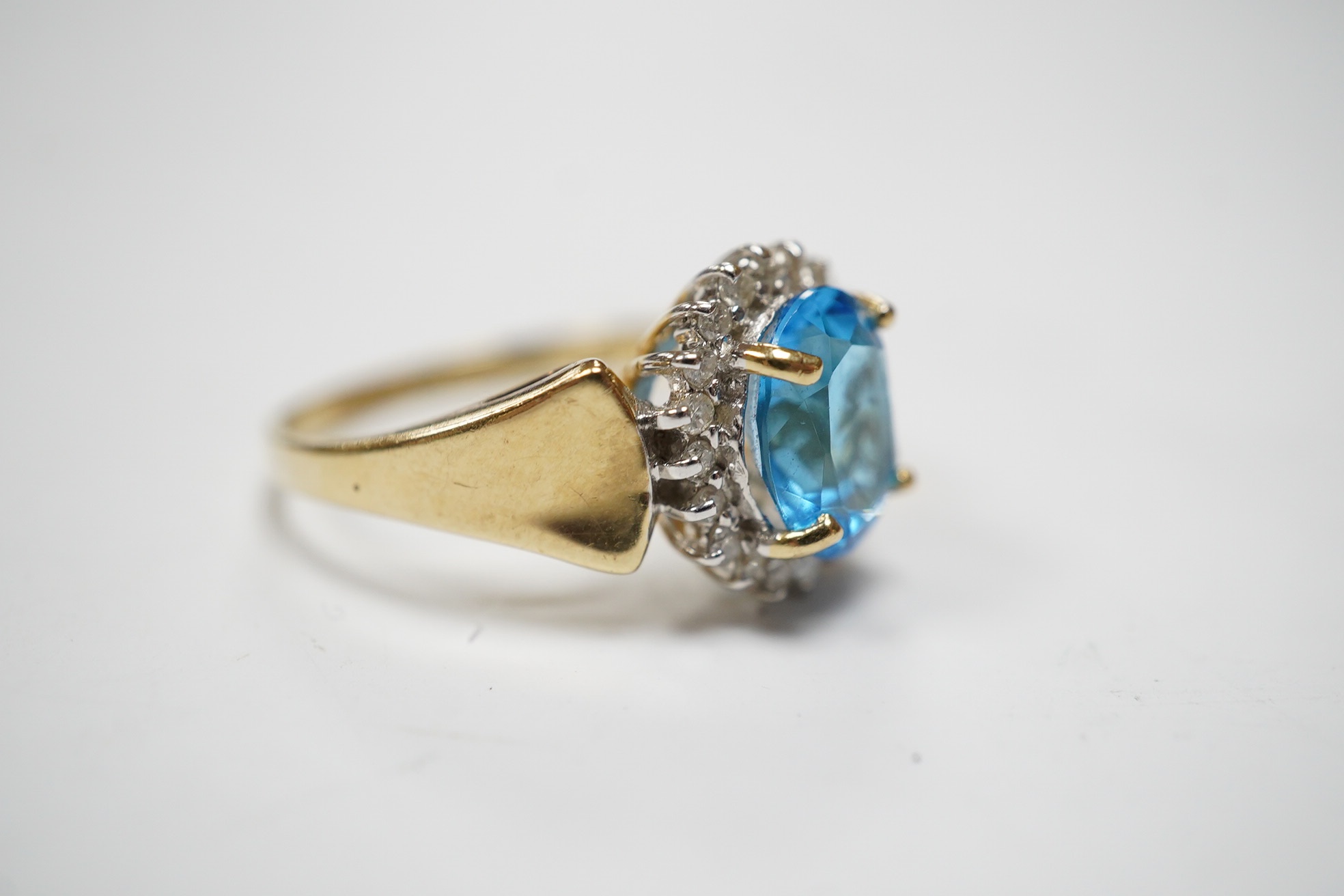 A modern 14k and oval cut blue topaz set dress ring, bordered with diamonds, size R, gross weight 4.7 grams. Condition - fair to good.